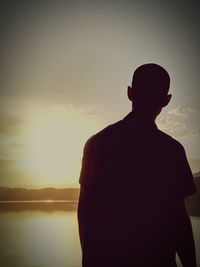 Rear view of silhouette man by sea against sky during sunset