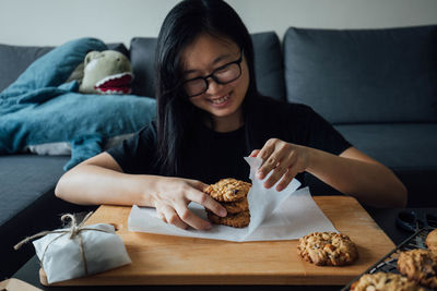 Young woman wrapping cookie while sitting by table at home