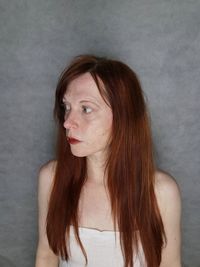 Woman looking away while standing against wall