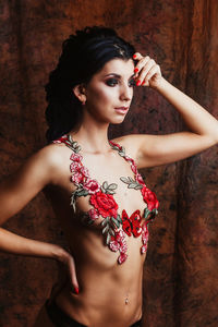 Shirtless young woman with floral decoration standing against wall