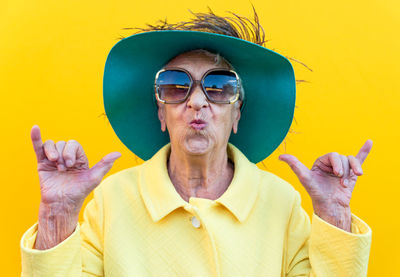 Portrait of senior woman gesturing against yellow background