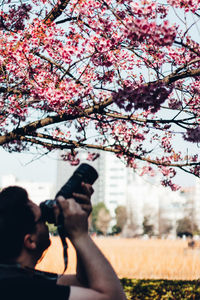 Low angle view of man photographing through flower tree