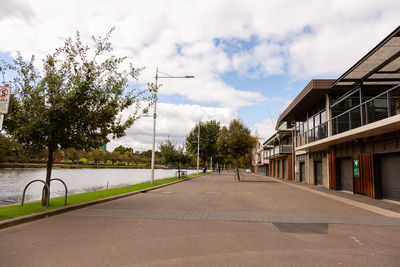 Empty road amidst trees and buildings against sky