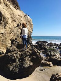 Rear view of woman standing on rock formations at beach