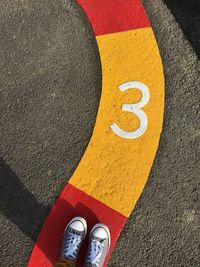 Low section of person standing on road marking with number 3