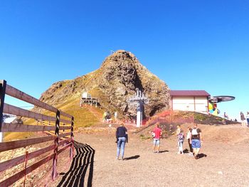 People walking on mountain against clear blue sky