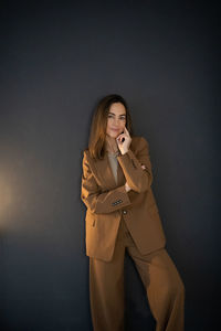 Young women in the braun suit near a dark gray background in thinking pose