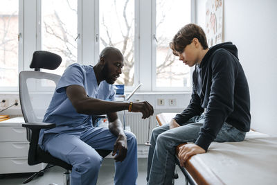 Male doctor checking knee of boy with reflex hammer in medical examination room