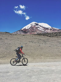 Man riding bicycle on mountain against blue sky