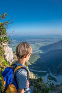 Rear view of boy looking at mountains against clear blue sky