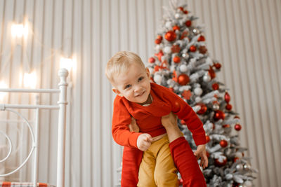 Cute smiling little son having fun in his father arms over christmas tree background