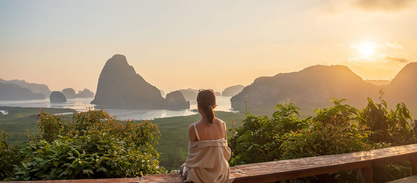 Rear view of woman standing by mountain against sky during sunset