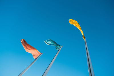 Low angle view of flags with colours against blue sky