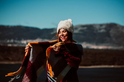 Smiling young woman standing against sky during winter