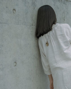 Rear view of young woman wearing chain while leaning on wall