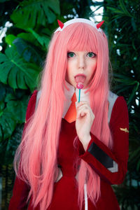 Portrait of beautiful young woman holding lollipop while standing against plants