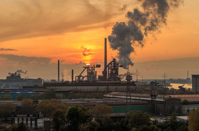 Smoke emitting from factory against sky during sunset