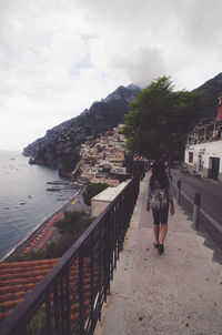 Rear view of woman standing on retaining wall by sea against sky