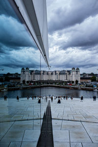 People by river in city against buildings and sky