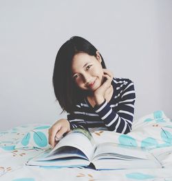 Portrait of young woman reading book while sitting on bed at home