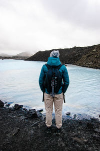 Rear view of man standing at hot spring against sky