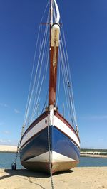 Sailboat moored on beach against clear blue sky