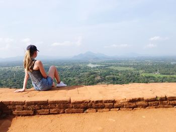 Woman sitting on mountain against sky