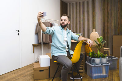 Mature man using mobile phone while unpacking things from boxes moving in new apartment.