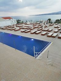 Lounge chairs by swimming pool at beach against sky