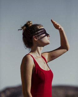 Young woman looking away while standing against sky