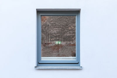 White house wall and window with reflection of red brickwall and green exit sign inside