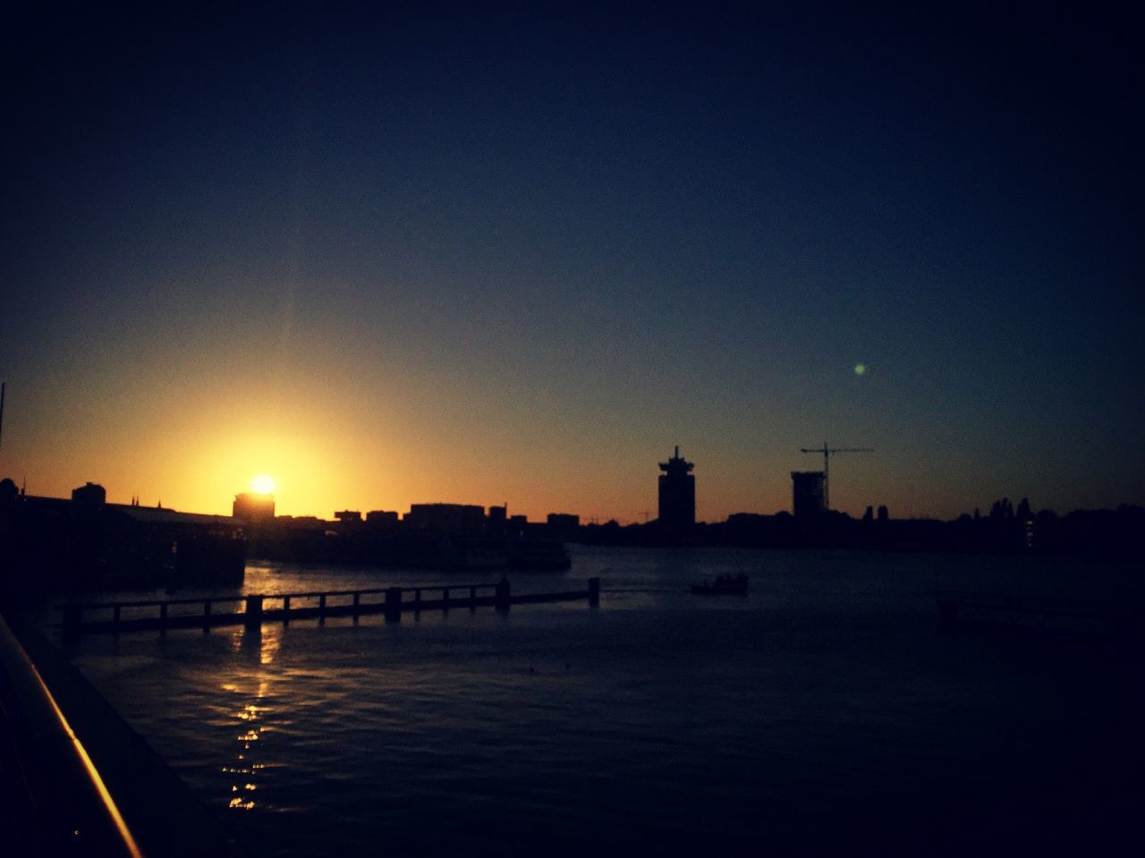 RIVER IN FRONT OF SILHOUETTE BUILDINGS AGAINST SKY AT SUNSET