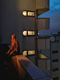 Woman standing by window in illuminated building