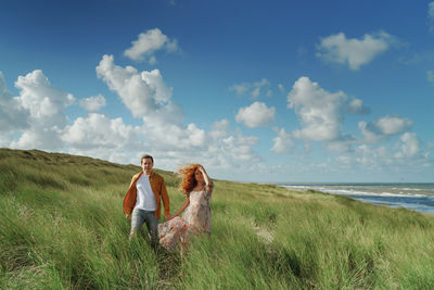 Couple on field by sea against sky