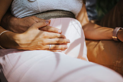 Midsection of pregnant woman with husband touching belly outdoors