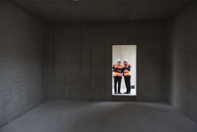 Two men wearing safety vests talking in building under construction