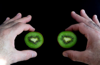 Close-up of hand holding fruit against black background