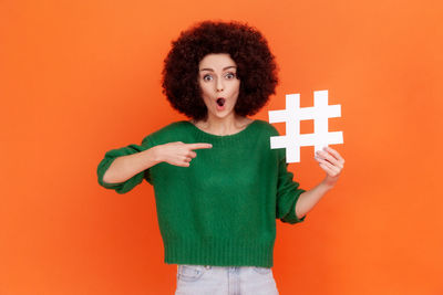 Portrait of surprised woman pointing at hashtag against colored background