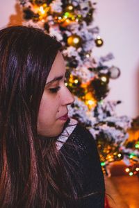 Close-up of woman sitting against christmas tree at home