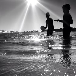 Low angle view of children playing in sea against sky on sunny day