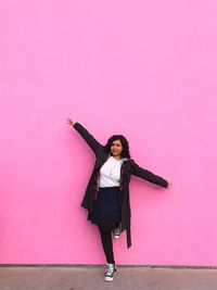 Full length of young woman with arms outstretched against pink wall