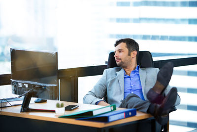 Full length of thoughtful businessman sitting at desk in office