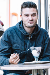 Portrait of smiling young man eating ice cream sitting at cafe
