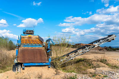 Old, mobile screen for gravel and sand in blue color standing on the field, in the background blue