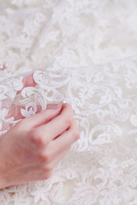 Cropped hand of woman stitching pearls on white wedding dress