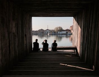 Rear view of friends sitting on pier against clear sky