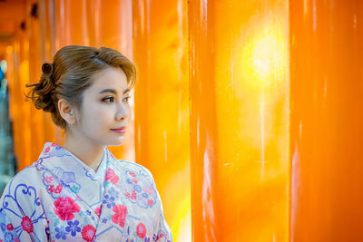 Portrait of smiling young woman standing against orange background