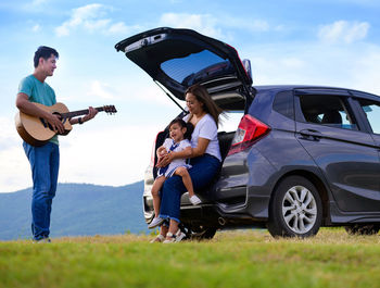 Cheerful family sitting by car trunk on field