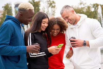 Friends looking at smart phone while standing outdoors