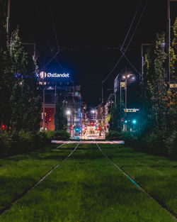 Illuminated street amidst buildings against sky at night